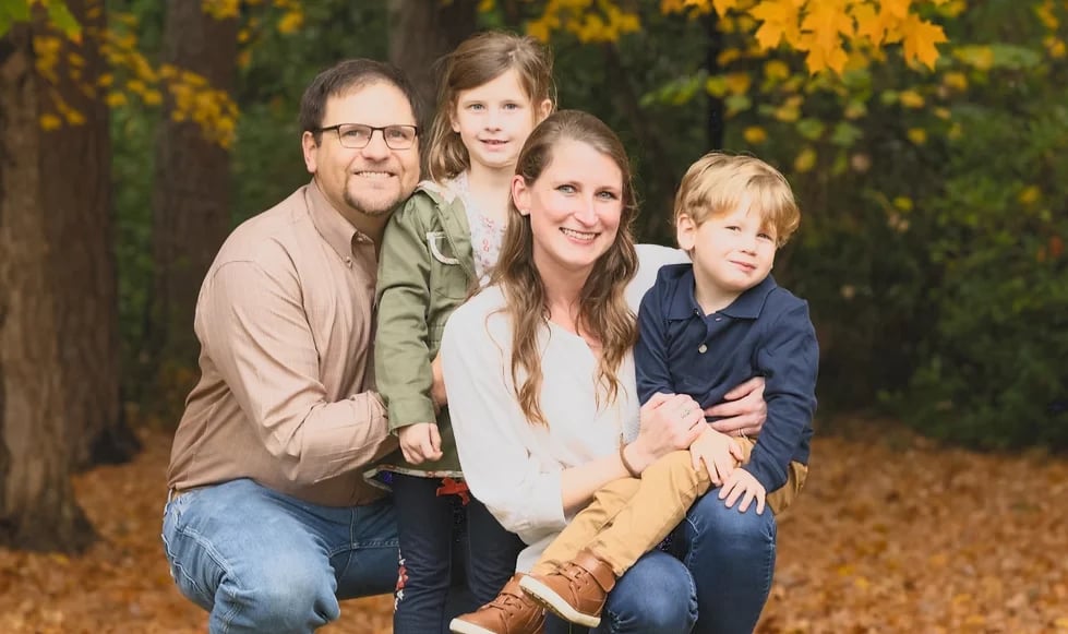 Family of four posing together outdoors in autumn setting with fall foliage in background